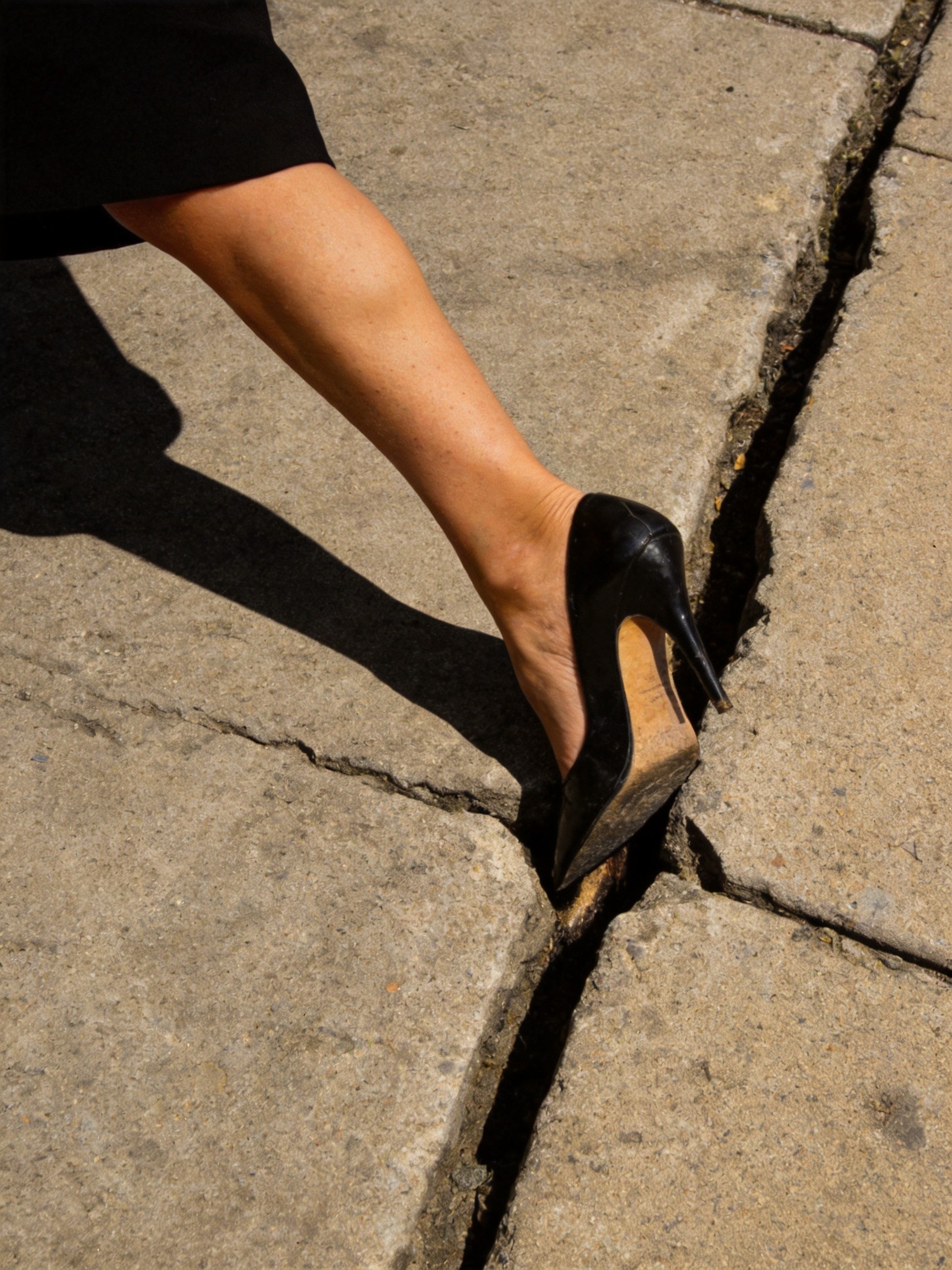 Comparison of three heel geometries on a city sidewalk with a metal grate, showing a stiletto heel wedged into a grate slot at left, a tapered block heel at the grate edge at center, and a wide low block heel sitting safely on top of the grate at right