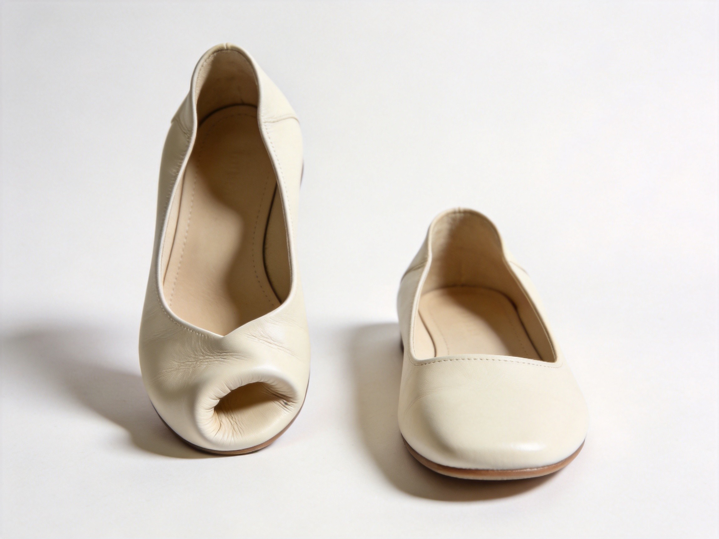A side-by-side product comparison photograph on a clean white background, on the left a cream leather flat shoe showing a pronounced upward curl at the toe box with the front of the shoe visibly bent up creating a ski-tip deformation, on the right an identical cream leather flat shoe with a perfectly flat horizontal toe box profile lying flush with the surface in pristine unworn condition, illustrating the dramatic difference between toe-box deformation failure and intact flat construction